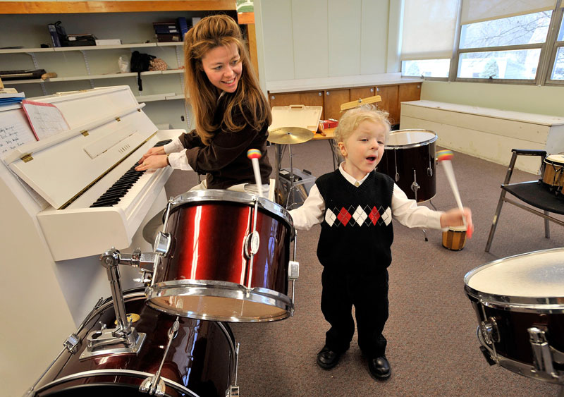 A woman playing the piano and a boy playing the drums.